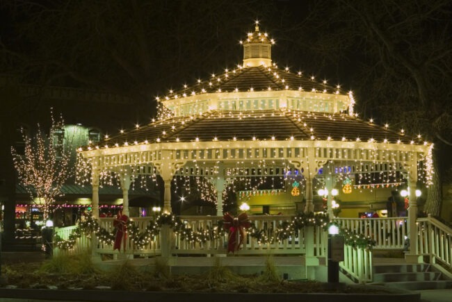 An illuminated gazebo adorned with festive lights and significant decoration, set against a night backdrop, conveying a charming holiday atmosphere.