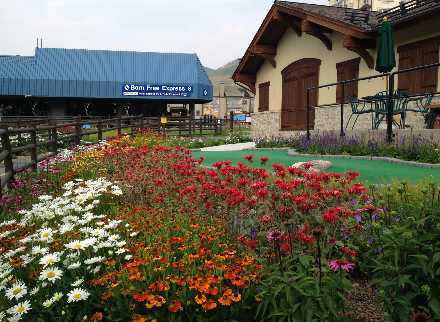 A colorful flower bed in the foreground with a chairlift station labeled 