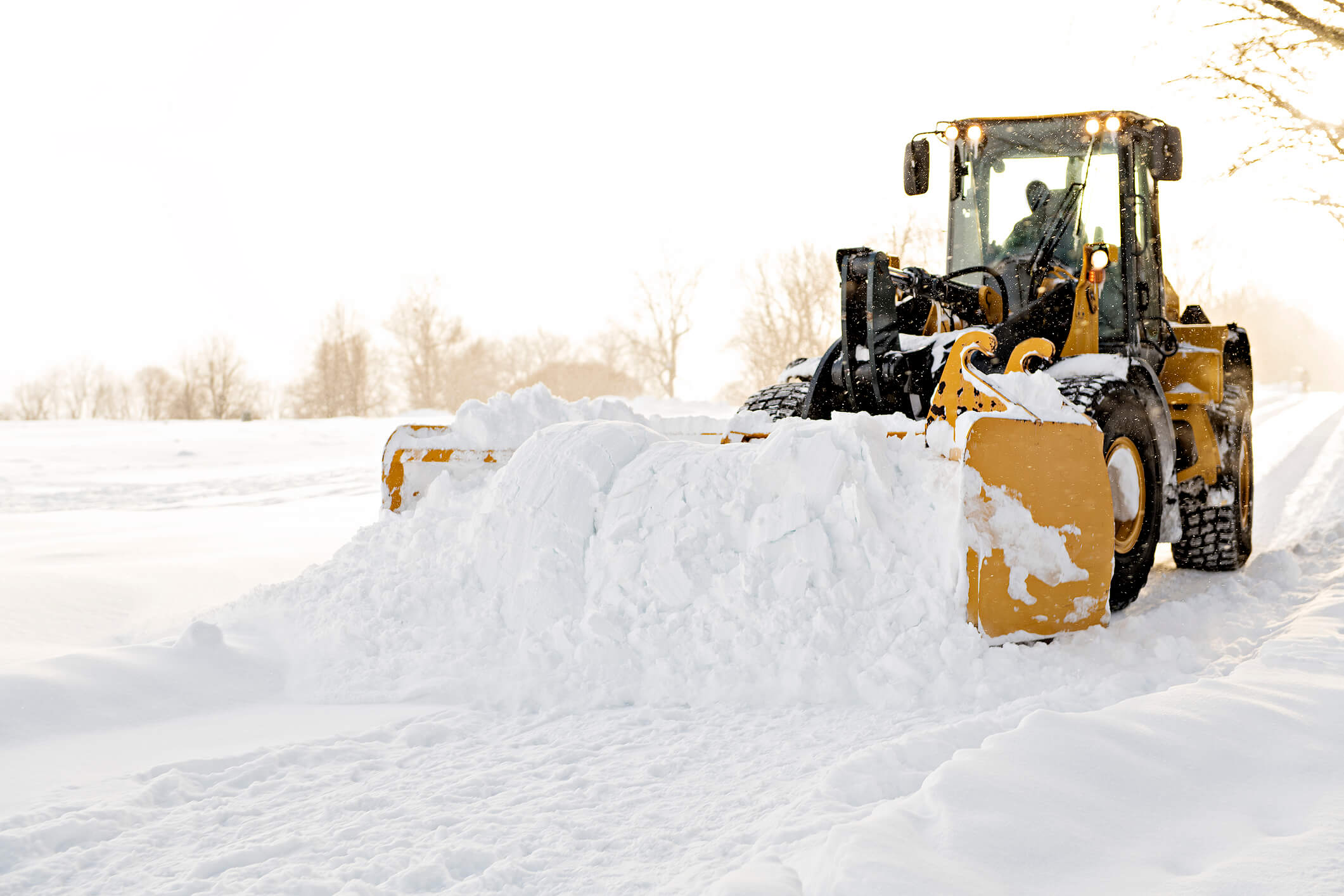 A large commercial snowplow pushing through heavy snow on a road, showcasing efficient winter property maintenance.